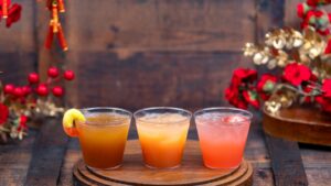 Bountiful Valley Cocktail Flight, three cocktails on a round wooden board, one garnished with a peach gummy ring and one with a strawberry