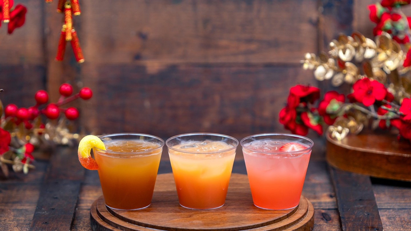 Bountiful Valley Cocktail Flight, three cocktails on a round wooden board, one garnished with a peach gummy ring and one with a strawberry
