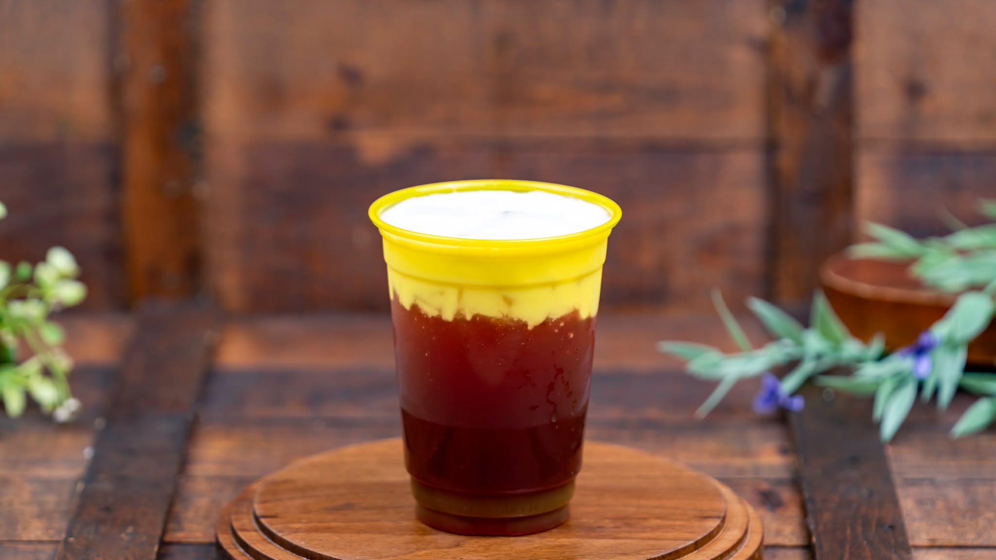 Vodka Pomegranate-Blueberry Martini, a dark red drink under a layer of foam in a yellow-rimmed cup on a wooden board