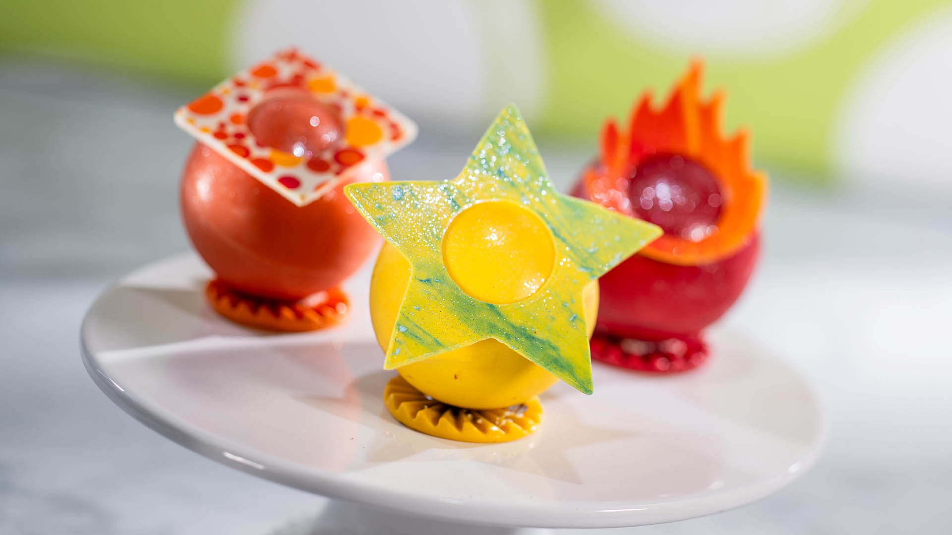 Orange, yellow and red Inside Out chocolate spheres on a cake stand, decorated with a square, a star and a flame