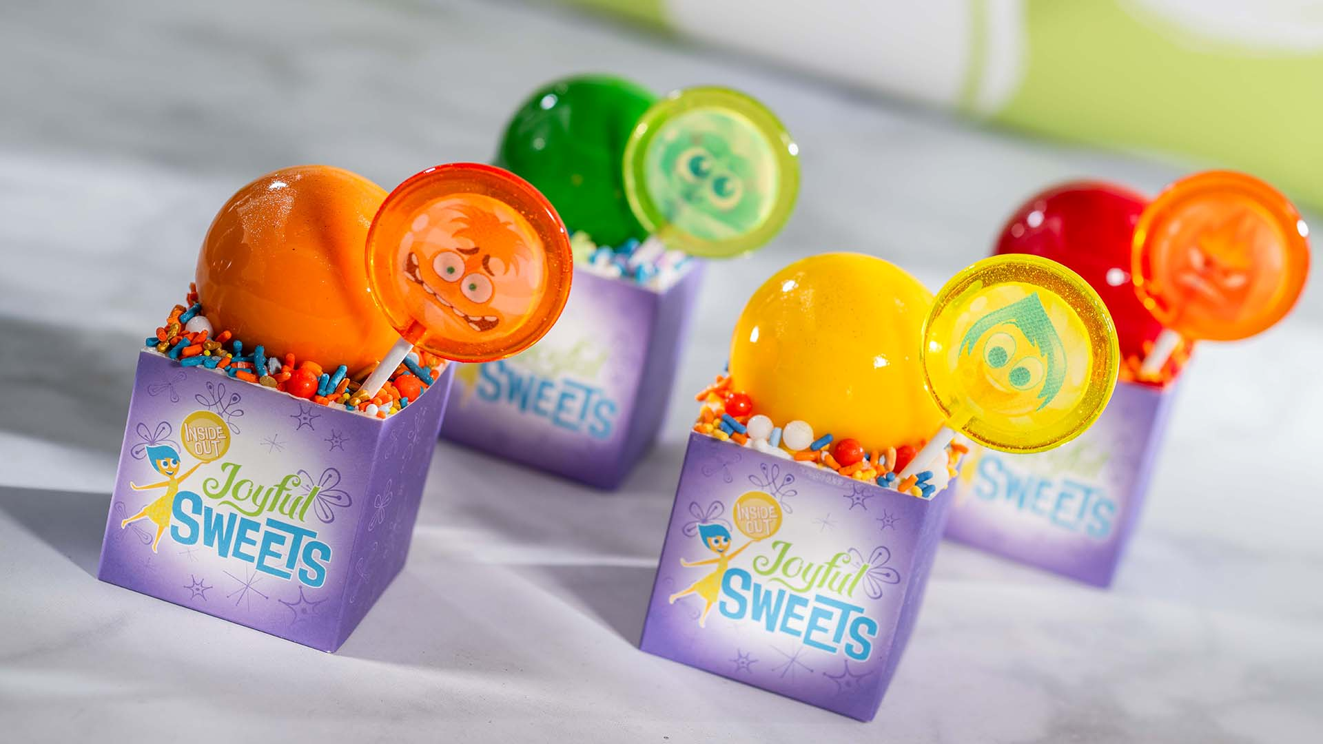Four Inside Out cupcakes in Joyful Sweets boxes, each topped with a character lollipop