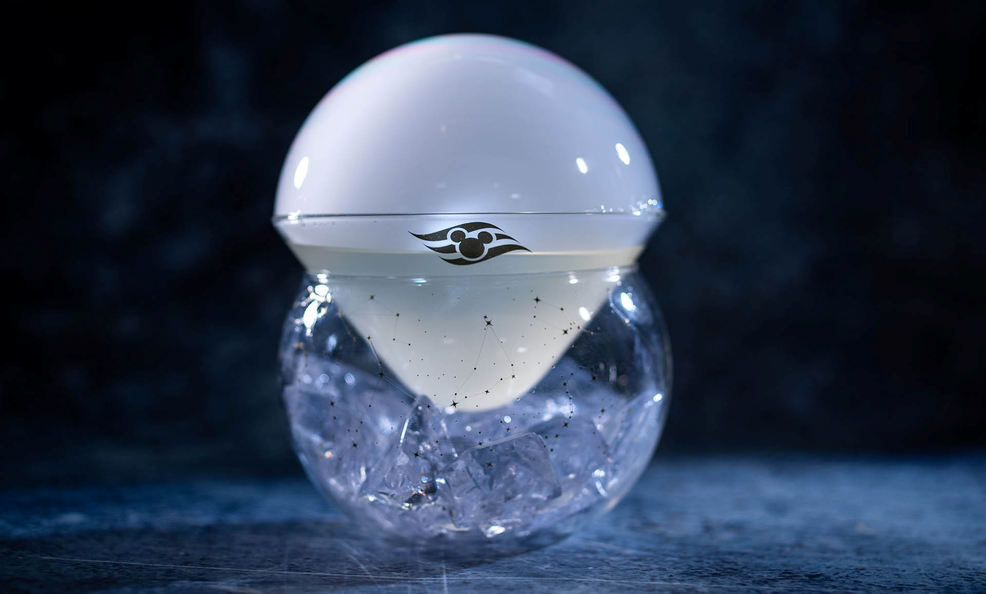 The Moonshine cocktail topped with a white aroma bubble in a speckled glass over ice, coming to Skygazers on the Disney Believe