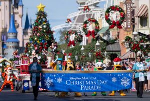 The Disney Parks Magical Christmas Day Parade banner carried down Main Street U.S.A. at Magic Kingdom ahead of Pluto, Daisy Duck, Donald Duck, the Mad Hatter, Alice and Tigger, with Mickey and Minnie Mouse on a Christmas tree float and Cinderella Castle behind