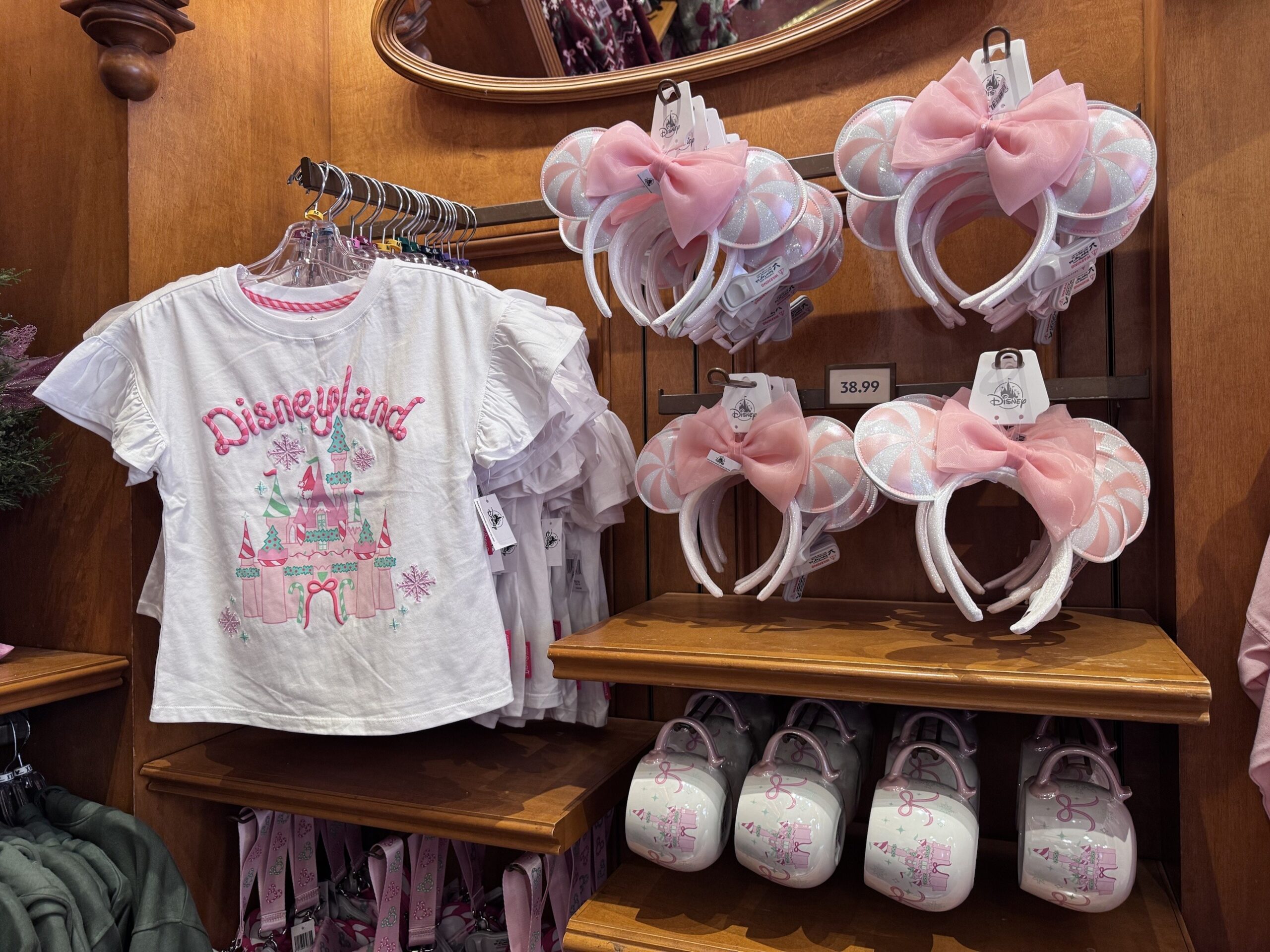 White ruffle-sleeve Disneyland castle tee next to pink and white peppermint swirl Minnie ears with pink bows priced $38.99 and castle mugs