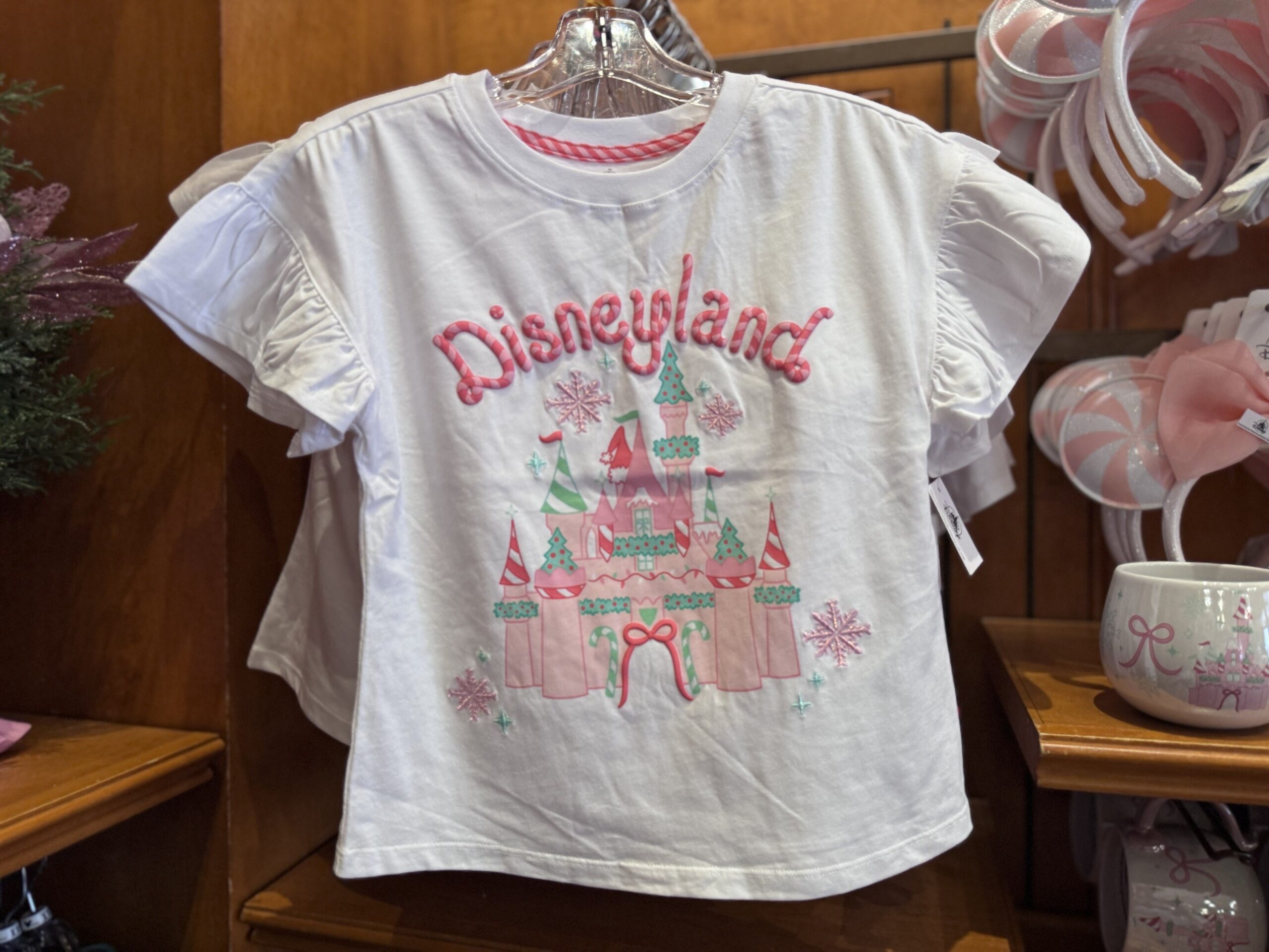 White ruffle-sleeve tee with puffy candy cane Disneyland lettering over a pink and mint holiday castle