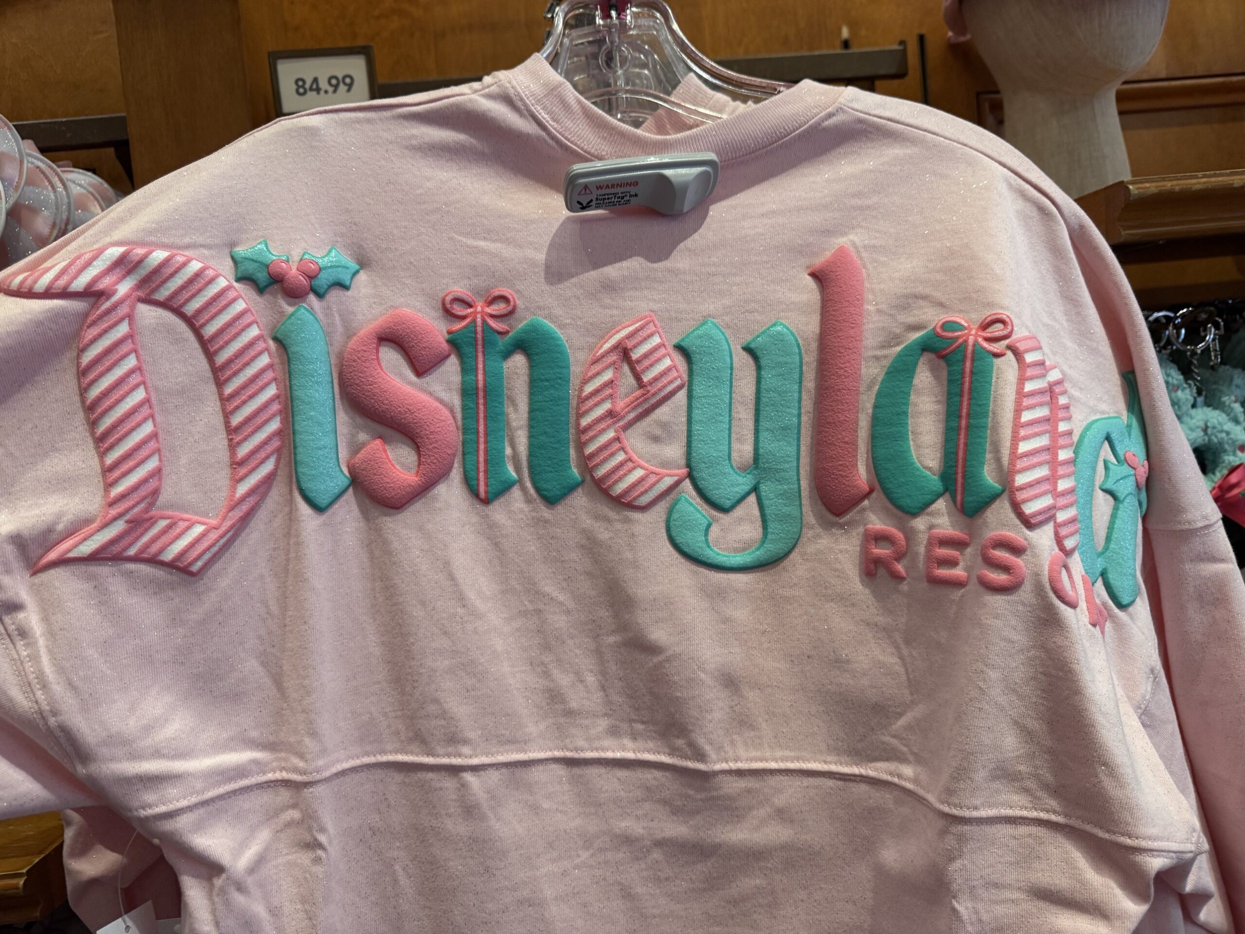 Pale pink long-sleeve top with puffy candy-striped, pink and teal Disneyland Resort lettering, holly and bows