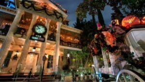 The Haunted Mansion at Disneyland at dusk, decorated with dark garlands, jack-o'-lanterns and a striped bow, with a clock counting days to Christmas above the entrance