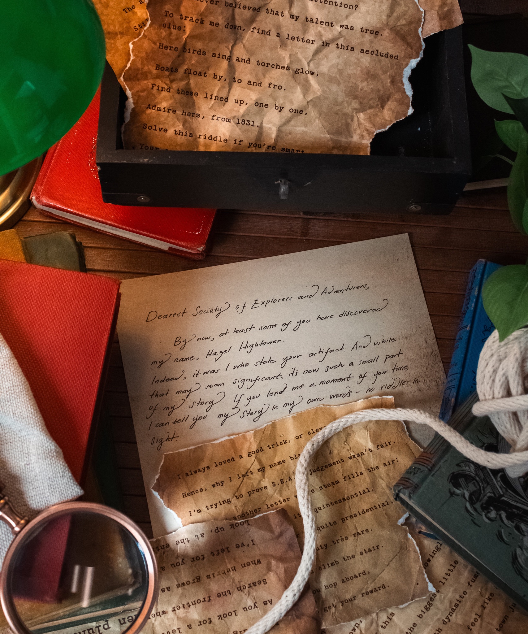 Handwritten letter from Hazel Hightower to the Society of Explorers and Adventurers surrounded by torn riddle pages, books and a magnifying glass