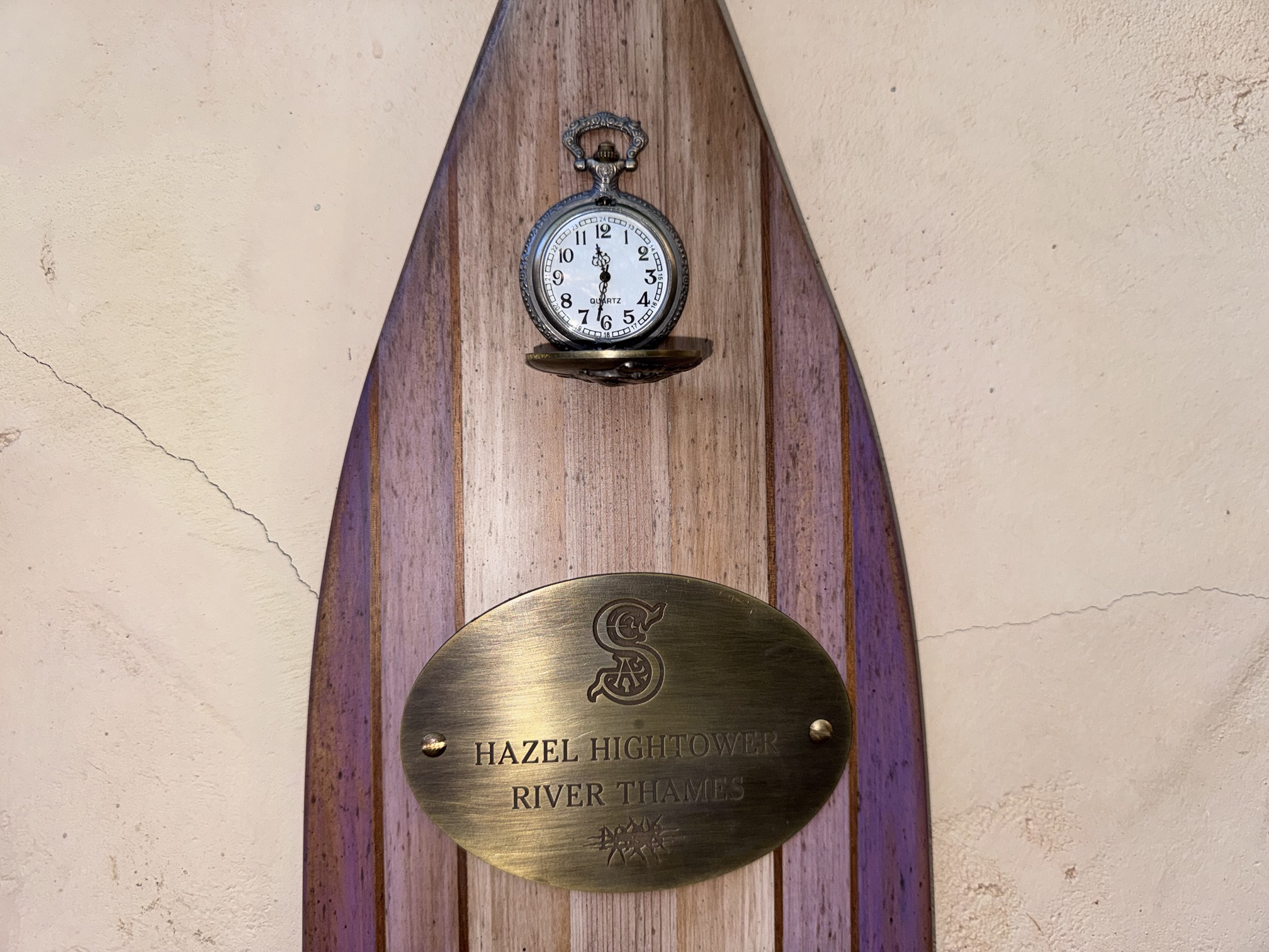 Hazel Hightower's purple striped oar with a pocket watch hanging beside other S.E.A. member oars at The Tropical Hideaway