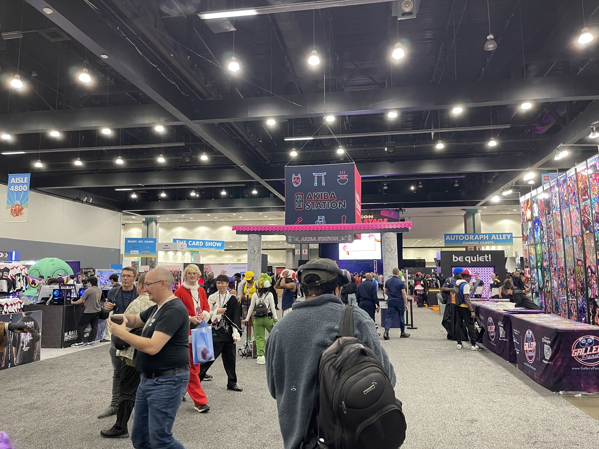 The Akiba Station sign hangs over the L.A. Comic Con floor near The Card Show and Autograph Alley signs as cosplayers pass by