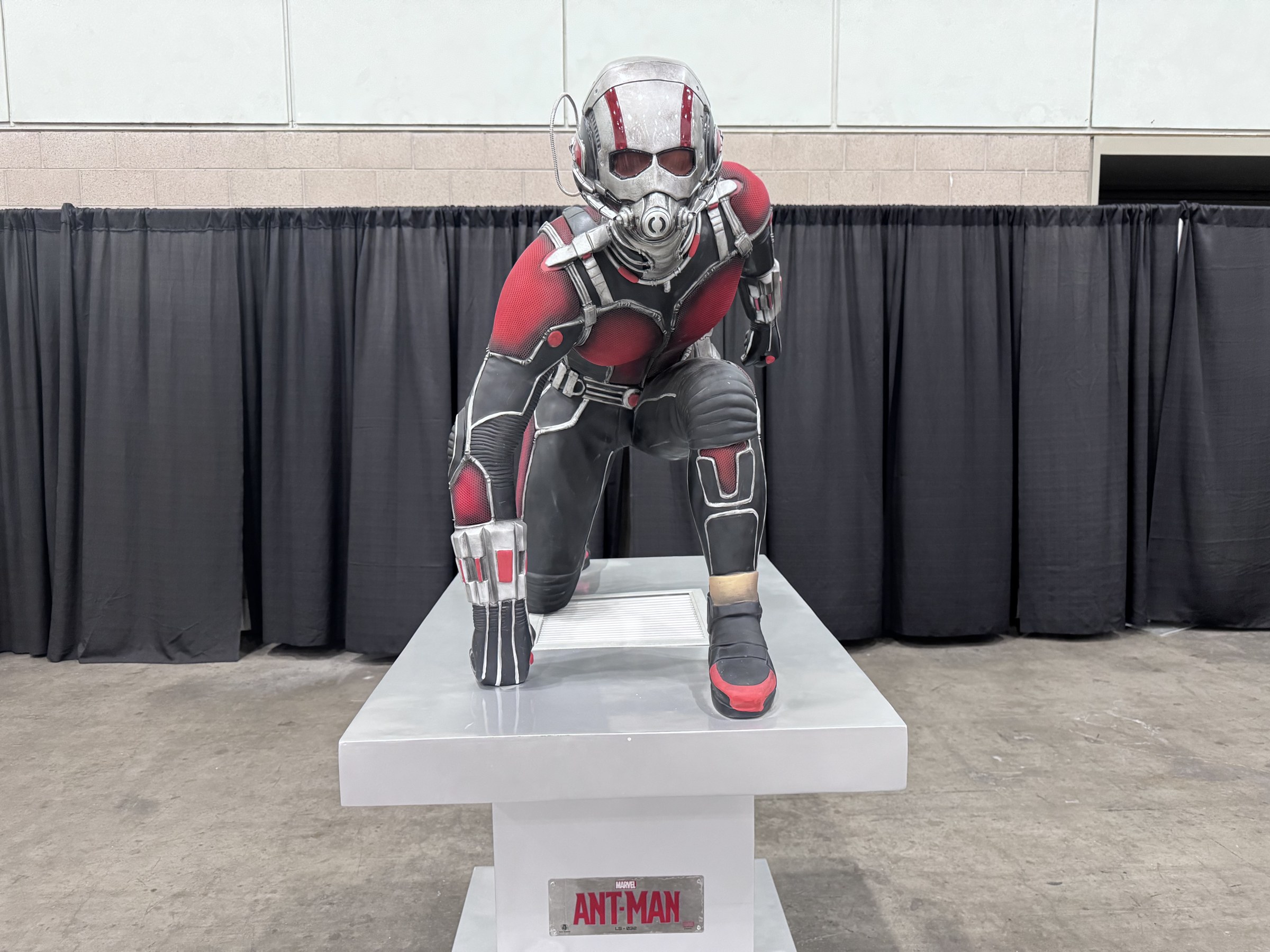 An Ant-Man statue crouched on a white pedestal labeled Ant-Man