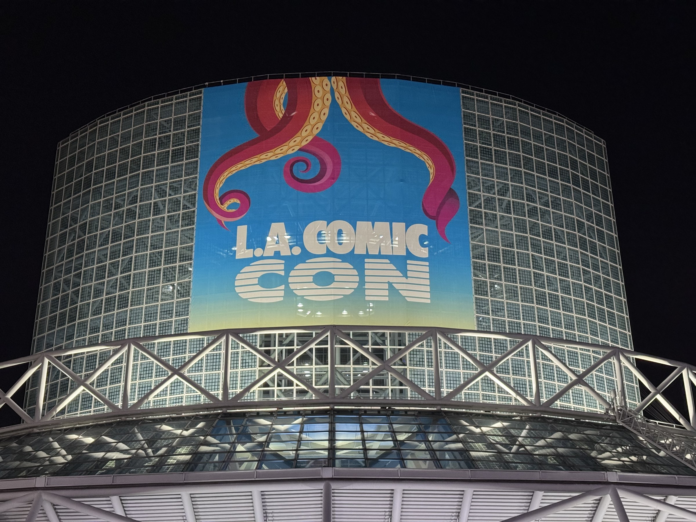 The L.A. Comic Con banner with red tentacle art on the convention center's glass tower at night