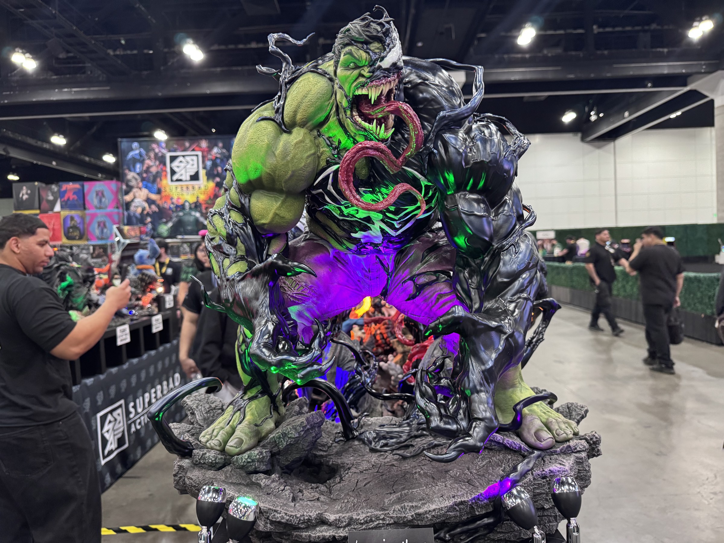 A lit-up Venomized Hulk statue with green and purple lighting at the Super Bad Action Figures booth
