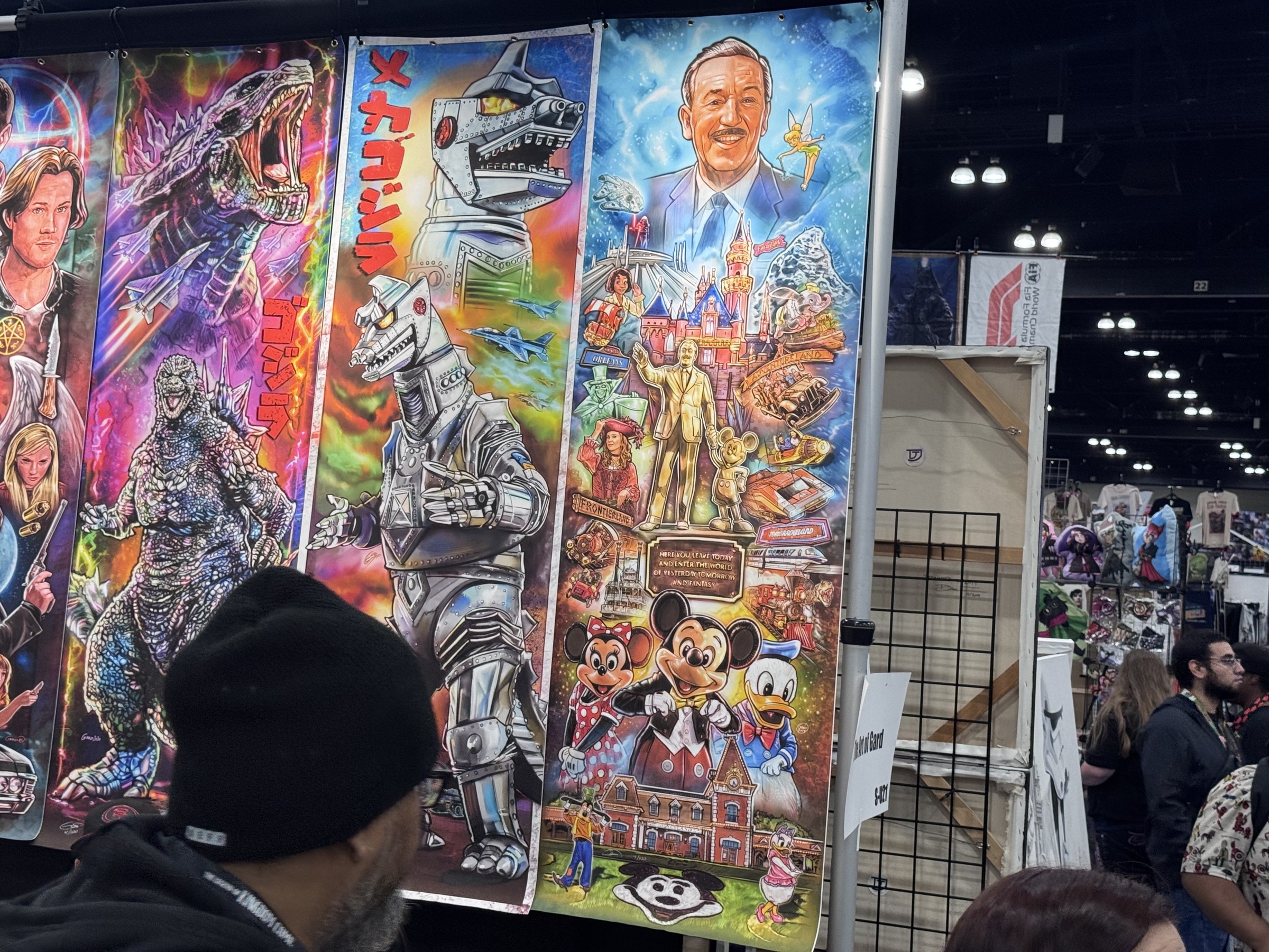An artist's print of Walt Disney over Disneyland landmarks, the Partners statue, Mickey, Minnie and Donald, hanging beside Godzilla and Mechagodzilla prints