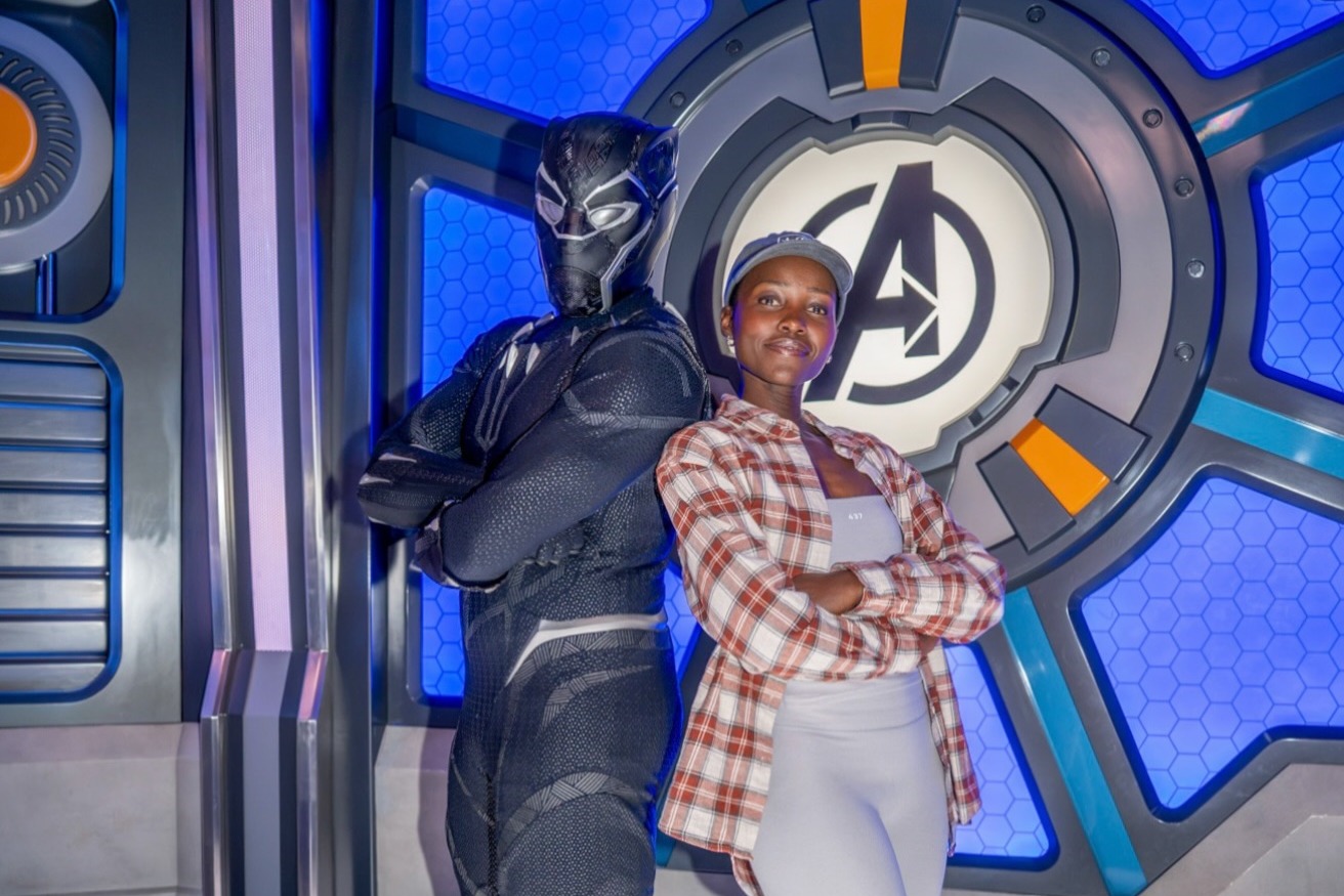 Lupita Nyong'o and Black Panther stand back to back with arms crossed in front of an Avengers logo at Marvel Avengers Campus in Disneyland Paris