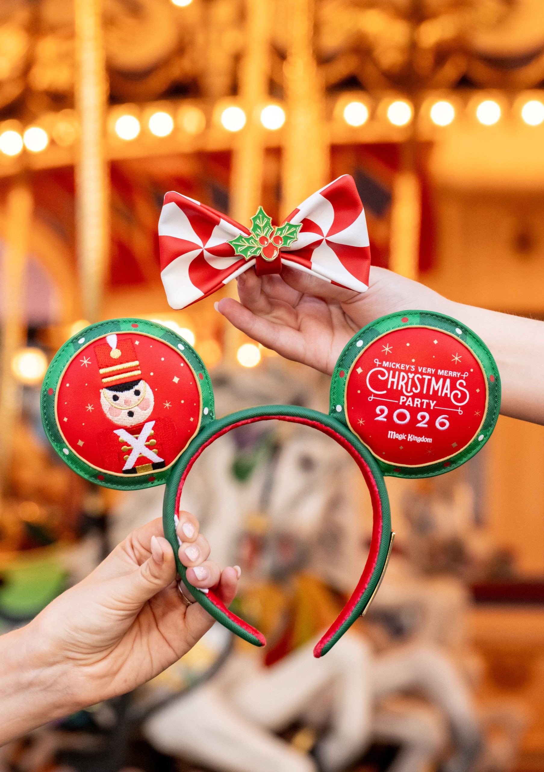 2026 Mickey's Very Merry Christmas Party ear headband in green and red with a toy soldier on one ear, the 2026 party logo on the other, and a red and white peppermint bow with holly