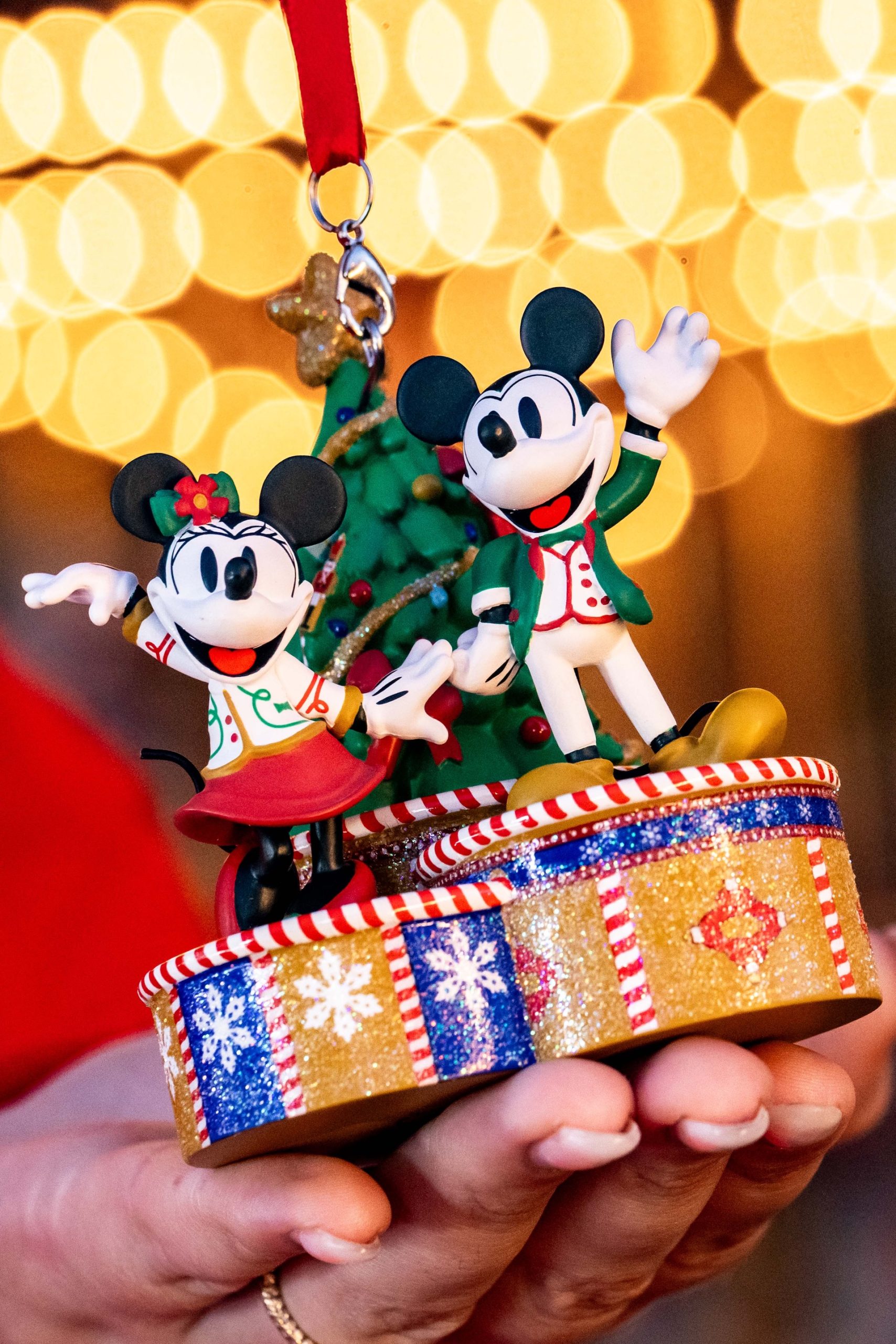 2026 Mickey's Very Merry Christmas Party ornament showing Mickey Mouse and Minnie Mouse in holiday outfits beside a Christmas tree on a glittery base with snowflakes and candy cane stripes