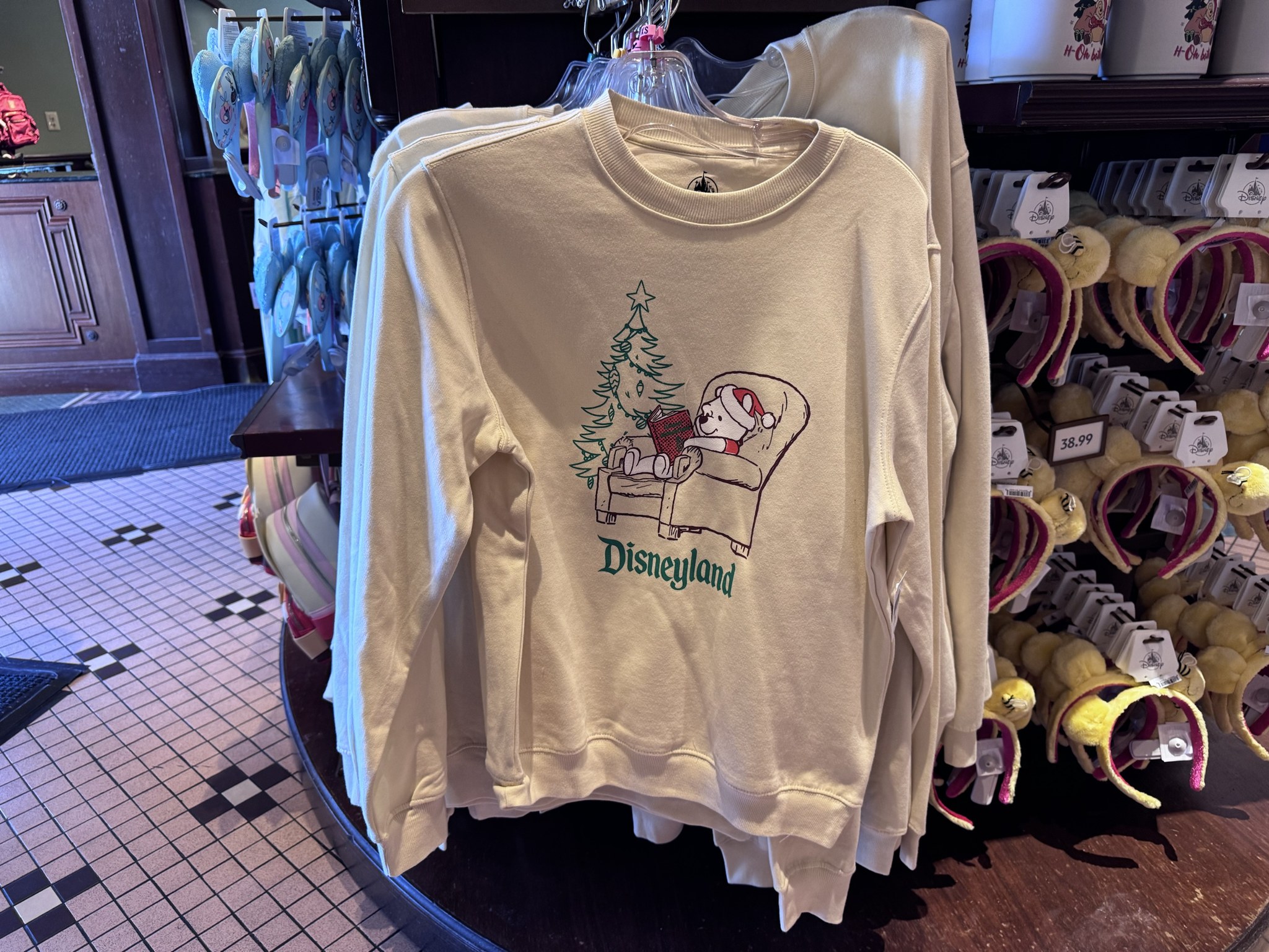 Cream Disneyland sweatshirt with a sketch of Pooh in a Santa hat reading a book in an armchair next to a Christmas tree