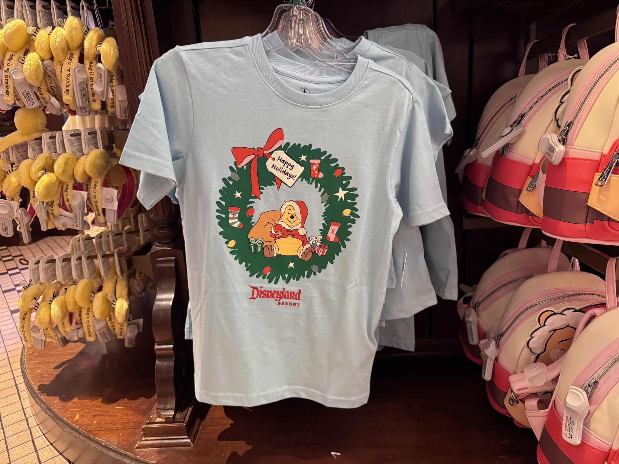 Light blue Disneyland Resort t-shirt showing Pooh in a Santa suit inside a wreath with a Happy Holidays tag and stockings lettered T, P and E