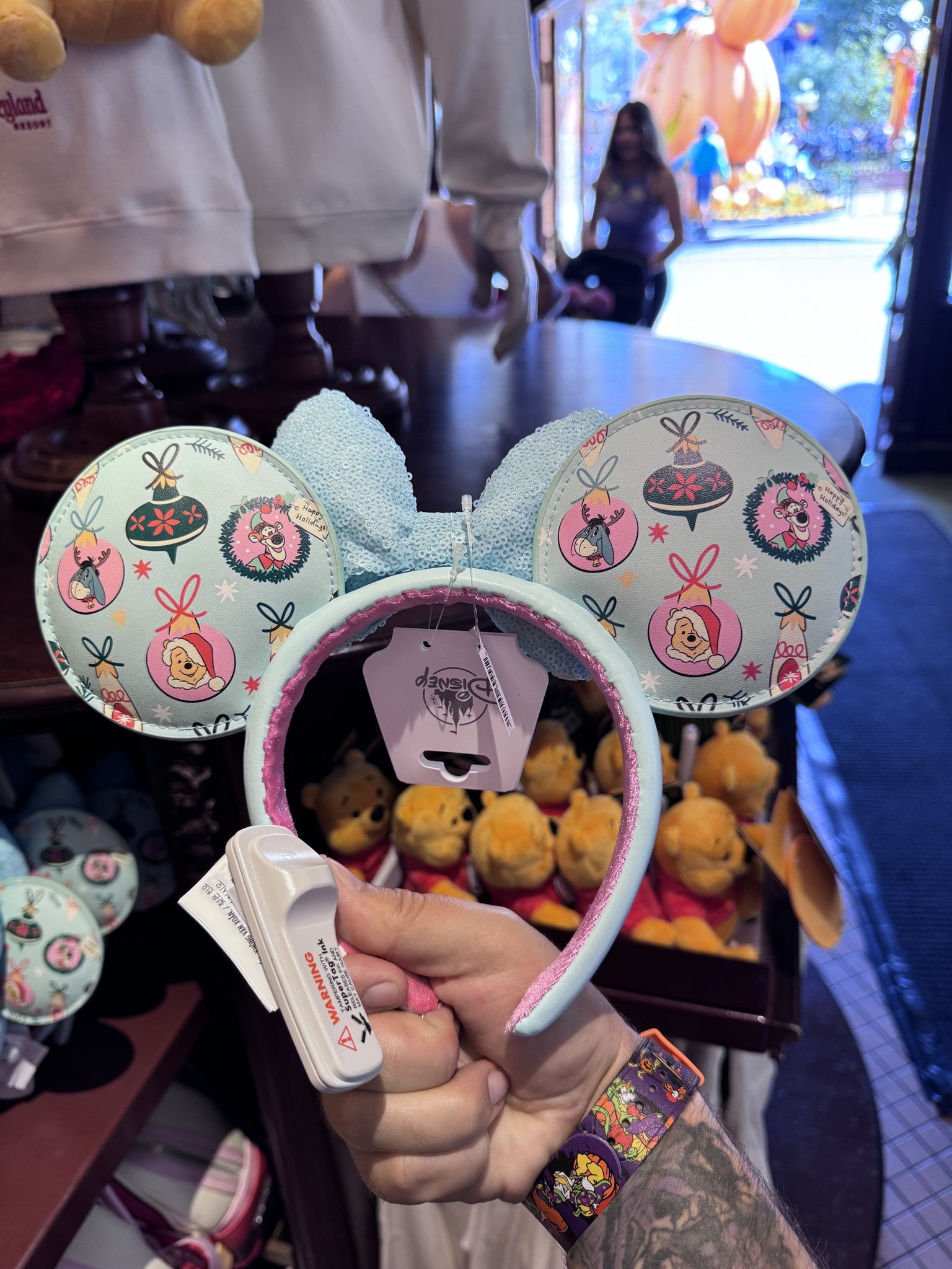 Mint Minnie ear headband printed with holiday ornaments showing Pooh in a Santa hat, Eeyore in antlers and Tigger in a wreath, with a light blue sequin bow and pink velvet band