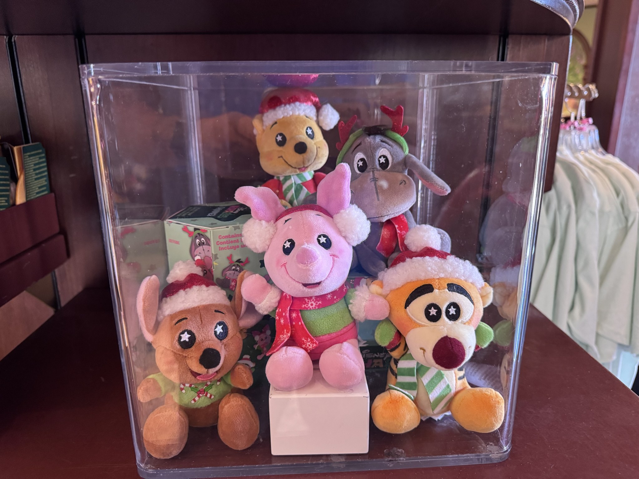 Display case of holiday Wishables plush of Pooh, Eeyore, Piglet, Roo and Tigger in Santa hats, scarves and antlers