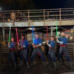 Five Saja in blue and gray robes with red sashes pose with lit lightsabers at night in Star Wars: Galaxy's Edge at Disney's Hollywood Studios