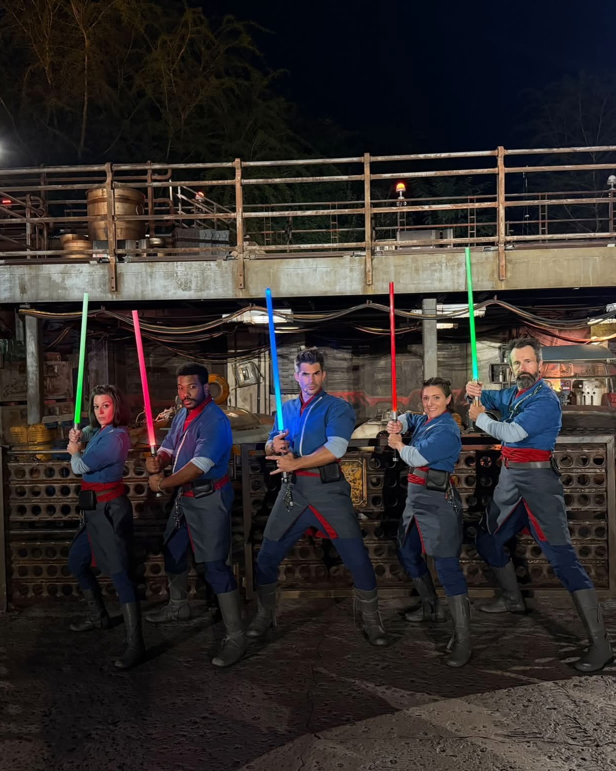 Five Saja in blue and gray robes with red sashes pose with lit lightsabers at night in Star Wars: Galaxy's Edge at Disney's Hollywood Studios