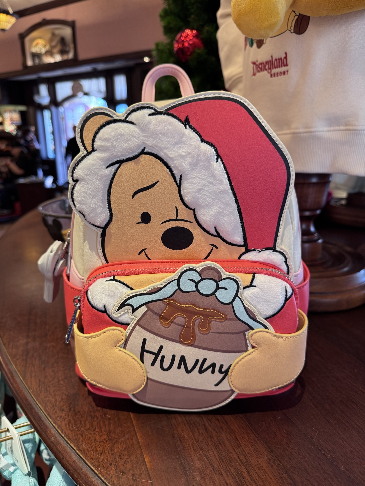 Mini backpack shaped like Winnie the Pooh in a Santa hat with fuzzy white trim, hugging a Hunny pot tied with a light blue ribbon