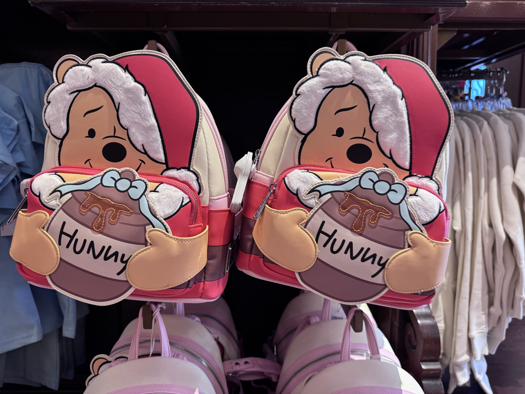 Two Santa Pooh Hunny pot mini backpacks hanging side by side on a wall display at the Emporium