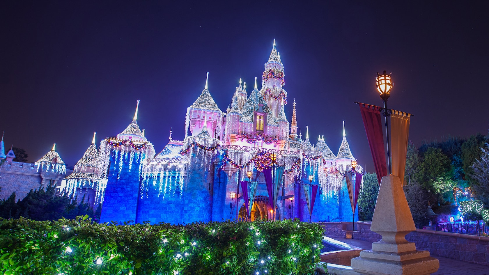 Sleeping Beauty Castle at Disneyland decorated for the holidays with icicle lights, garland and red and purple banners