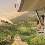 Guests in a suspended Soarin' ride vehicle with their feet dangling above a projected view of the Great Wall of China