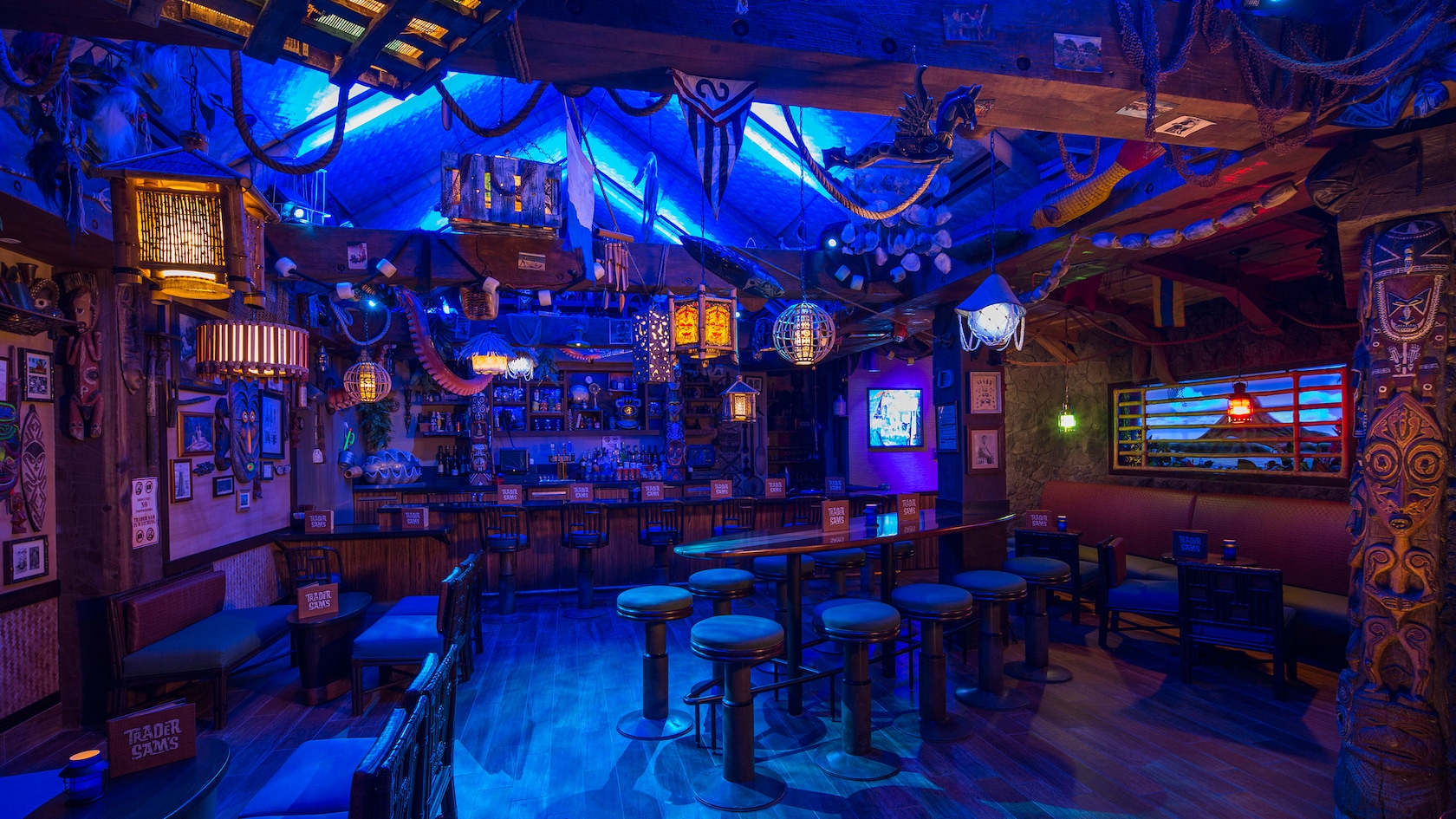 The bar and seating area inside Trader Sam's Grog Grotto, lit in blue with hanging lanterns and tiki carvings