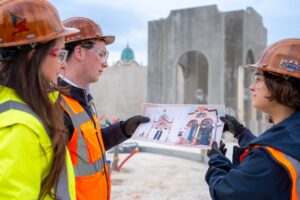 Imagineers in hard hats review Wilderness Explorers Sky Swings artwork on the construction site at Disney Adventure World